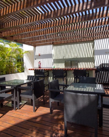 Covered terrace with wooden pergola, black wicker furniture, dining table, and potted palm plants