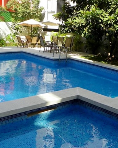 Rectangular swimming pool with spa tub, concrete deck, lounge chairs, umbrellas, and lush green landscaping