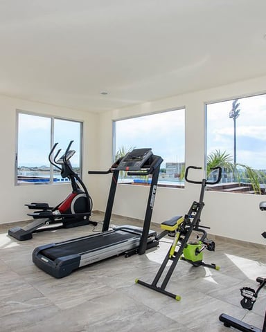 Bright fitness room with treadmill, stationary bikes, and elliptical machine overlooking marina and waterfront through large windows