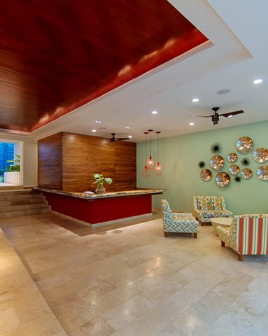 Modern lobby with red ceiling accent, wooden reception desk, mint green walls, decorative plates, and colorful patterned seating