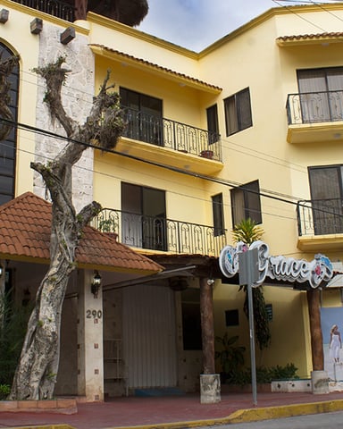 Yellow multi-story building with stone facade, balconies, and ground-floor storefront with ivy-covered tree.
