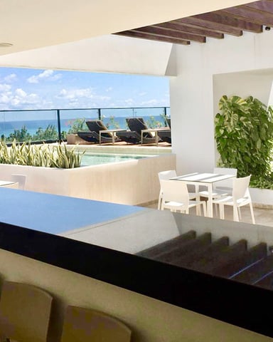 Modern rooftop terrace with ocean view, black kitchen counter, white dining chairs, pool, and lounge chairs