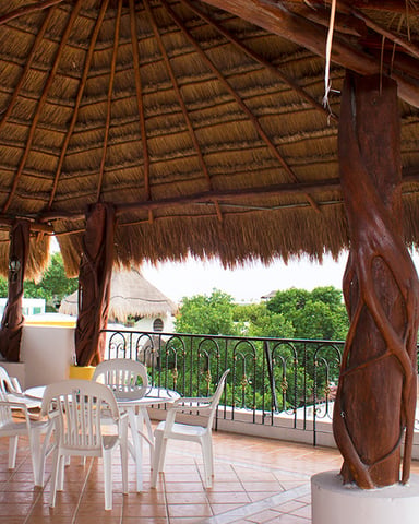 Rooftop terrace with thatched palapa, white lounge chairs and dining furniture, ocean and coastal town views