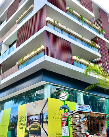 Modern apartment building with white and burgundy striped balconies, green plants, and ground-floor retail storefront with yellow signage
