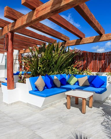 Rooftop patio with wooden pergola, blue built-in seating, potted plants, and clear blue sky