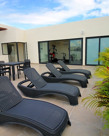 Modern terrace with lounge chairs, dining table, and tropical plants overlooking open landscape