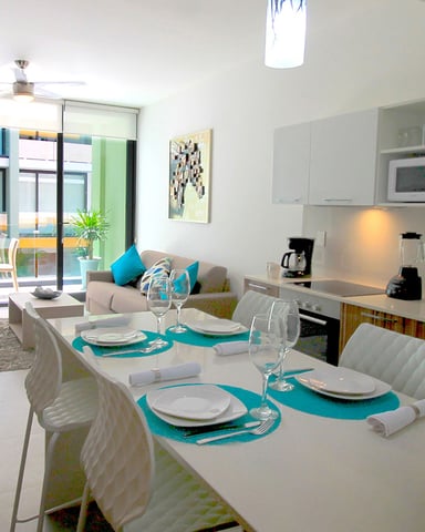 Open-plan kitchen and dining area with turquoise accents, white cabinetry, and sliding glass doors opening to balcony seating.