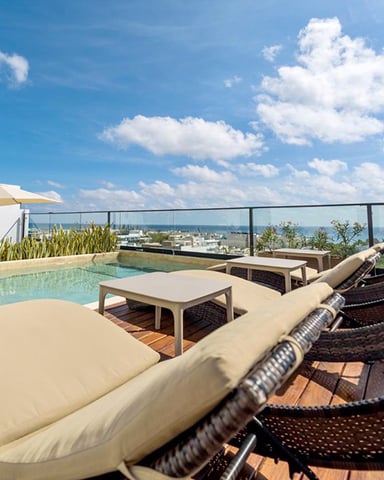 Rooftop terrace with lounge chairs, pool, umbrella, and panoramic city and water views under blue sky