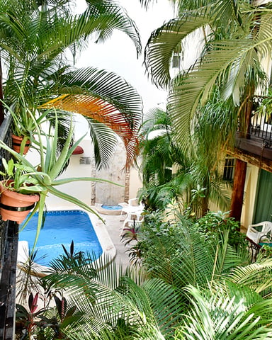 Tropical courtyard with blue swimming pool surrounded by lush palm trees and colonial-style buildings with balconies