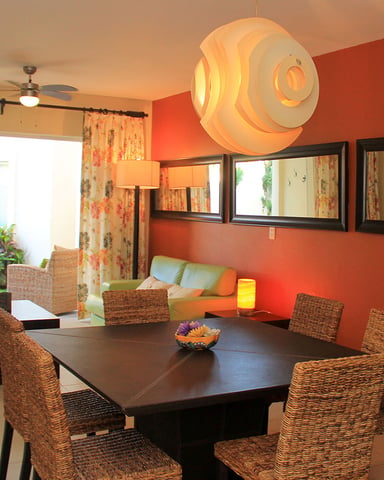 Open-plan dining and living room with red accent wall, black dining table, woven chairs, and view to patio