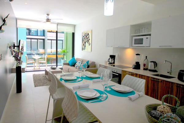 Open-plan kitchen and dining area with turquoise accents, white cabinetry, and sliding glass doors to balcony