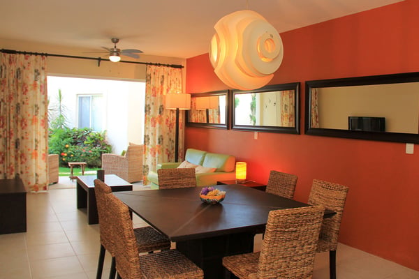 Dining room with red walls, black table, woven chairs, and open view to patio and living area