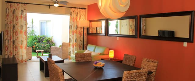 Open-plan dining and living room with red accent wall, woven chairs, black table, and view to patio