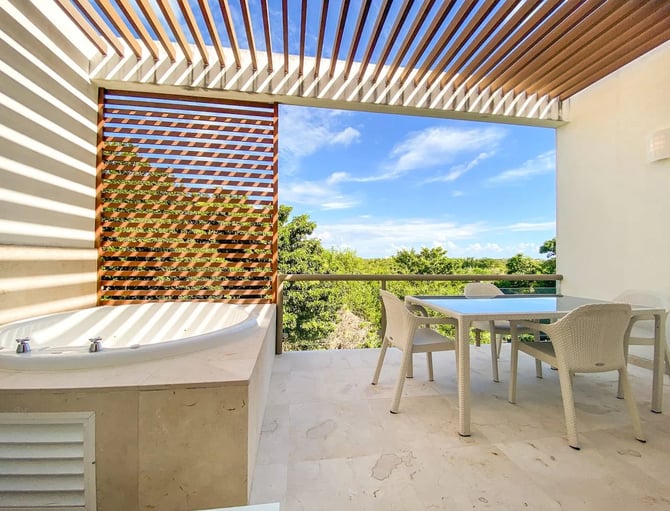 Modern terrace with soaking tub, dining table, woven chairs, wooden pergola, and views of lush landscape and pool